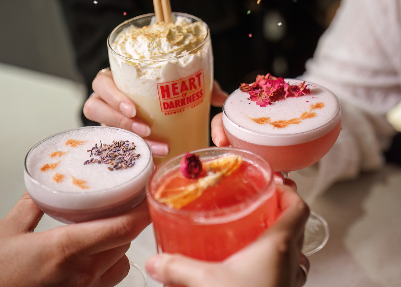Four people holding Heart of Darkness cocktails with colorful toppings in a festive setting.